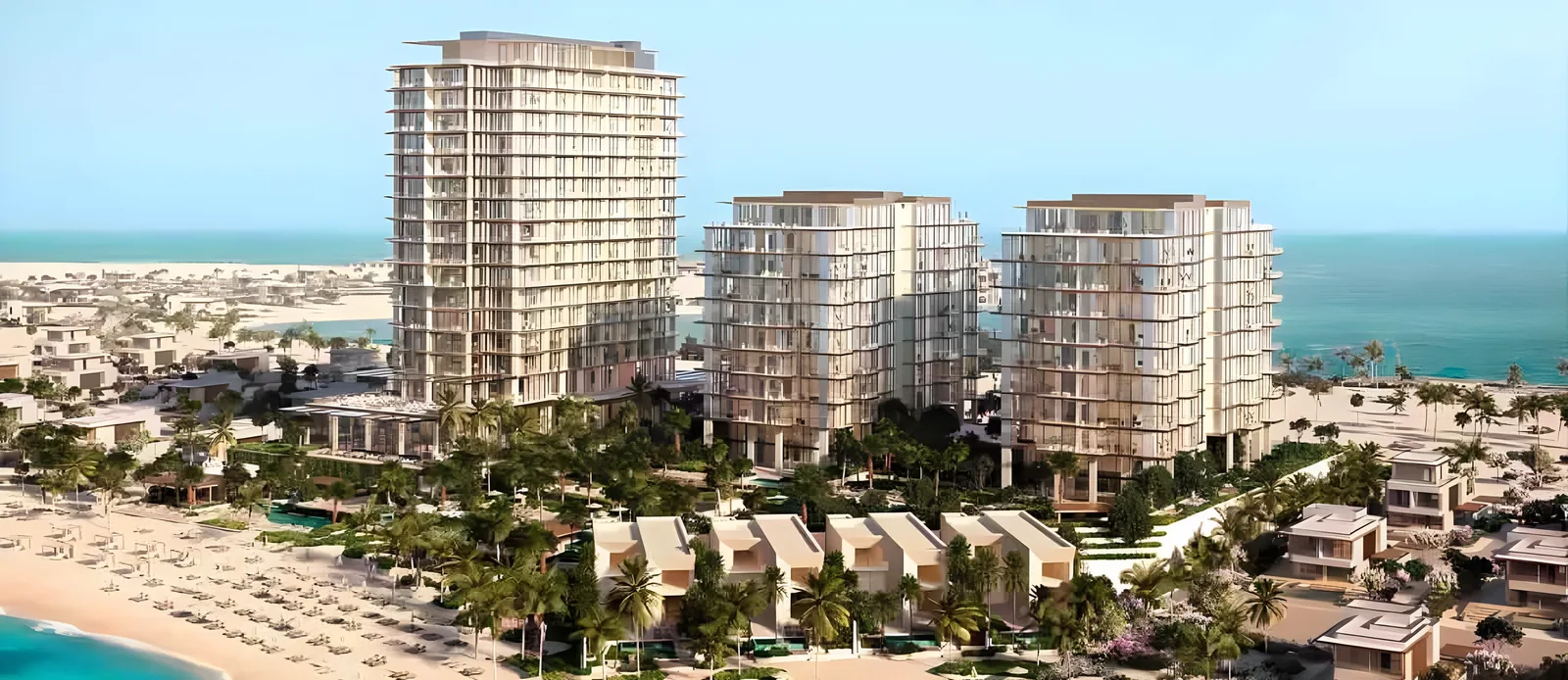 Aerial view of three tall beachfront residential towers with lighter mid-rise buildings and low-rise villas, surrounded by palm trees, swimming pools and gardens, with a sandy beach lined with umbrellas and turquoise water under a clear sky.