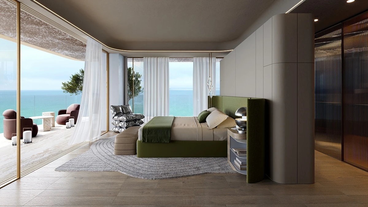 Contemporary bedroom with a green padded bed, gray round rug, floor to ceiling windows, and a balcony with pink armchairs facing the sea.