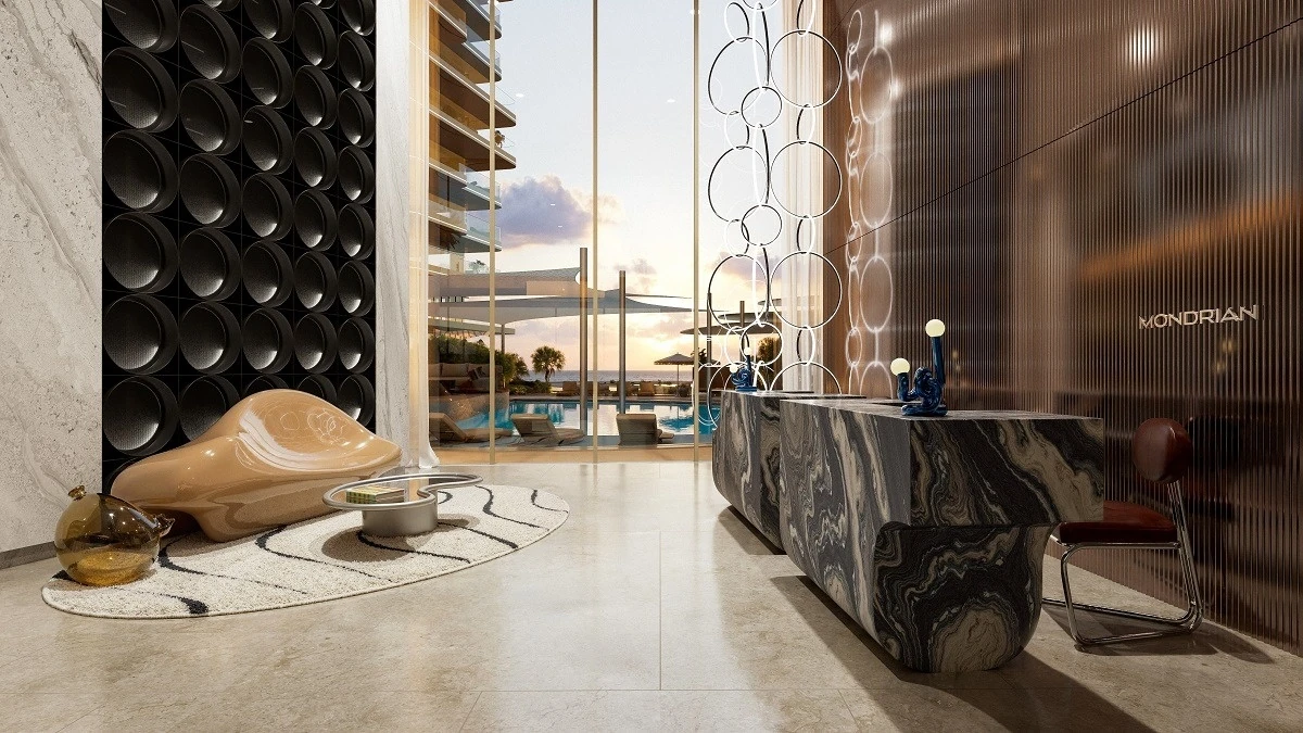 Contemporary hotel lobby with a swirled marble reception desk, curved beige sculptural bench, textured black wall panels, and large windows showing a pool and ocean at sunset.