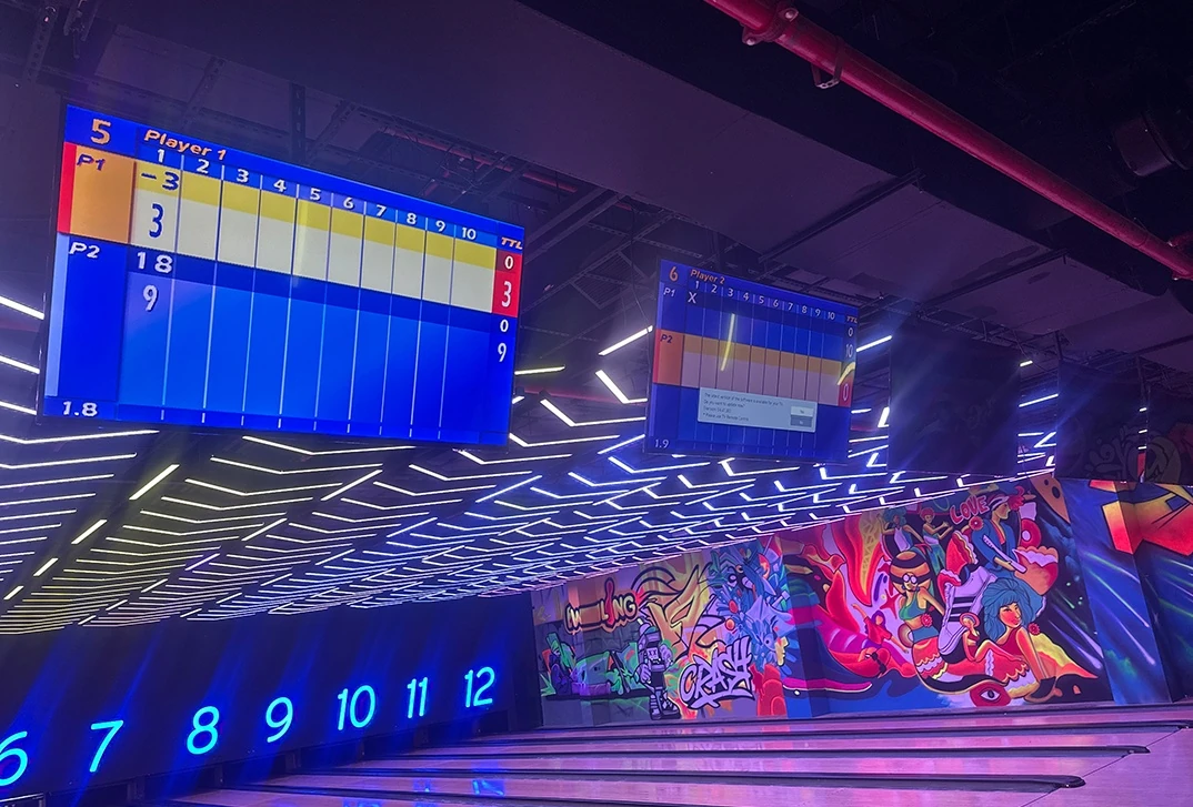 Too Hot Outside? Try These 7 Indoor Activities in Ras Al Khaimah this Long Weekend, Ras Al Khaimah: Two blue digital bowling scoreboards mounted overhead show Player 1 and Player 2 frames, with glowing lane numbers 6 through 12 below and a bright