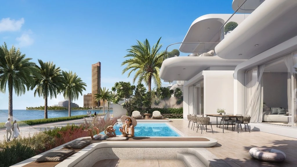 Oystra Al Marjan Island: A New Luxury Waterfront Development in Ras Al Khaimah, Ras Al Khaimah: Two people lounge by a small rectangular pool on the terrace of a white curved-architecture villa, with an outdoor dining table, palm trees, a