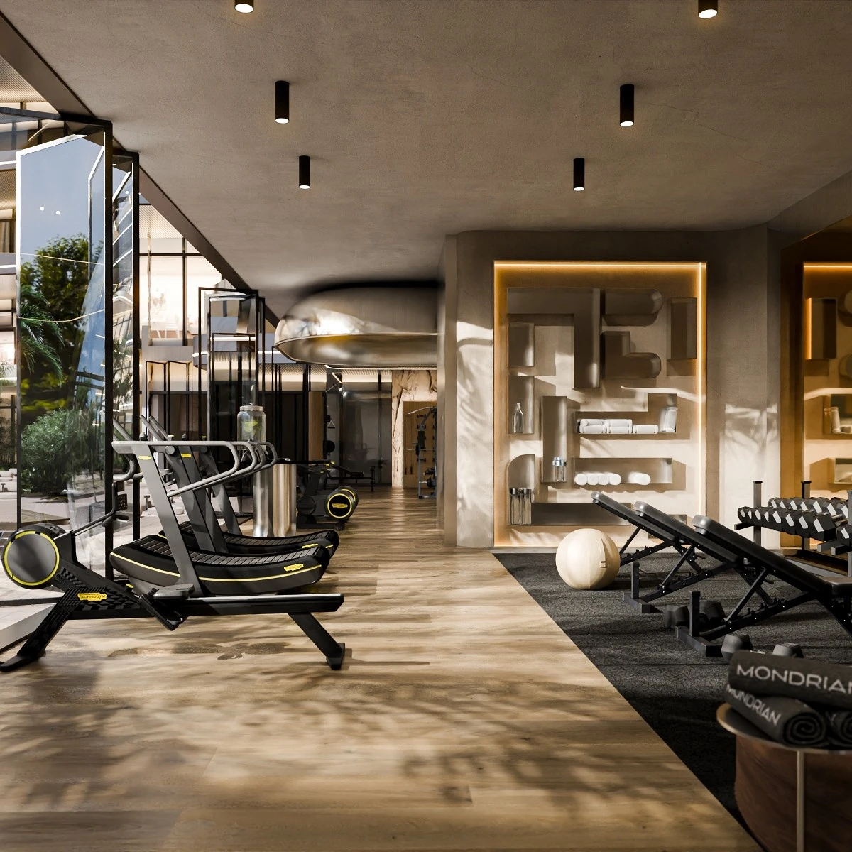 Upscale gym with black curved treadmills on wood flooring, adjustable weight benches and a dumbbell rack on grey carpet, wall shelving with rolled towels, folded towels branded Mondrian, exercise ball, glass wall with greenery, and cylindrical ceiling lights.